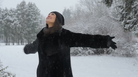 Beautiful woman is dancing in a winter park. It is snowing. She is happy in winter. Smiling. Slow motion. Winter park. Winter forest.