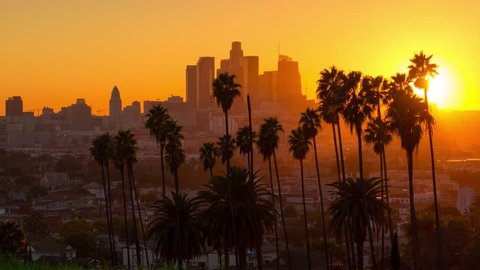 Scenic sunset to night transition zoom out from city of Los Angeles downtown skyline palm trees in foreground. 4K UHD timelapse.