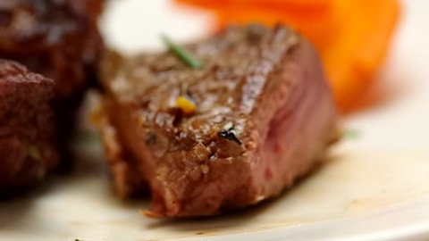 Knife cutting through delicious steak on white plate, blurry vegetable background