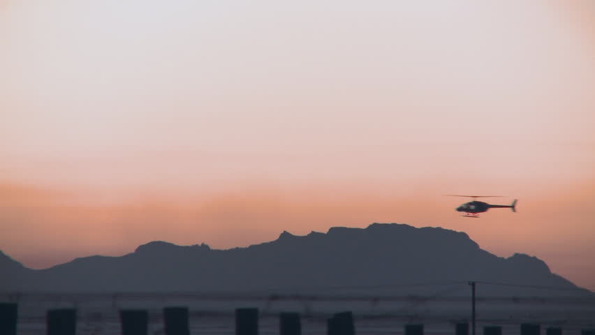 A helicopter moves slowly across a sunrise sky