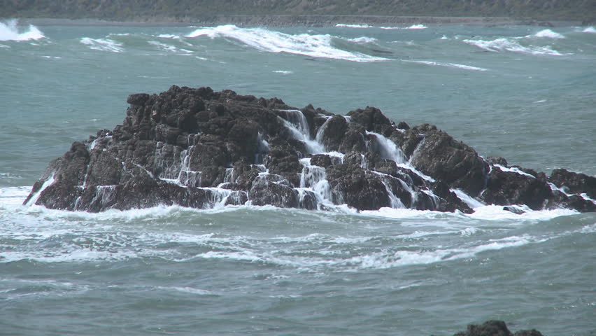 Large waves crash over some offshore rocks