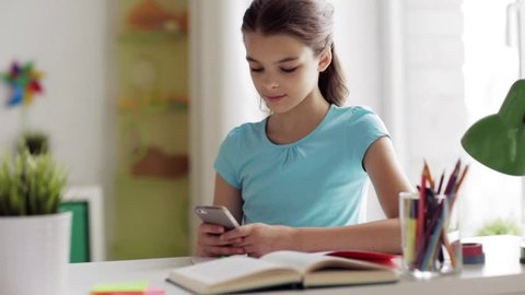 children, technology and communication concept - smiling girl distracting from homework and texting on smartphone at home
