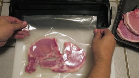 A man takes two pork chops wrapped in plastic. The chef takes the plastic bag and inserts it into a vacuum food sealer. The vacuum packer shrink wraps the raw meat in preparation for sous-vide cooking