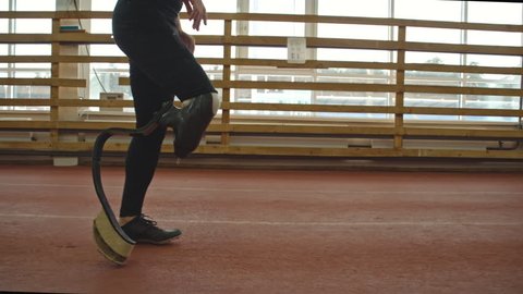 Low section tracking of amputee sportsman with prosthetic leg training on running track in slow motion at indoor stadium
