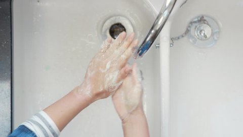 Directly above shot of woman washing hands with soap. Female is cleaning hands under running water of faucet. She is rubbing hands over sink in kitchen.