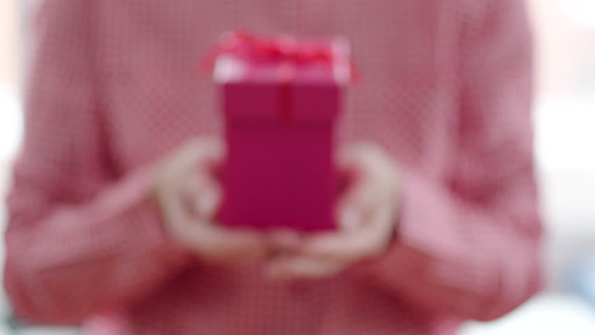 Close up of pink gift box with red ribbon in womans hands