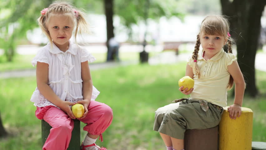 Two girls eating the apples in the playground