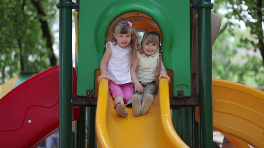 Two girls go down the slide on the playground