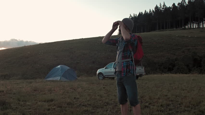 Young male hiking, 4x4 and trekking enthusiast, during leisure activities in mountains and looking with binoculars at view. 