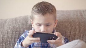 Boy playing game on smart phone sitting on sofa medium shot