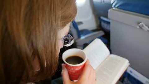 Woman drinking hot coffee while flying in private jet - reading captivate book till the landing at the next destination