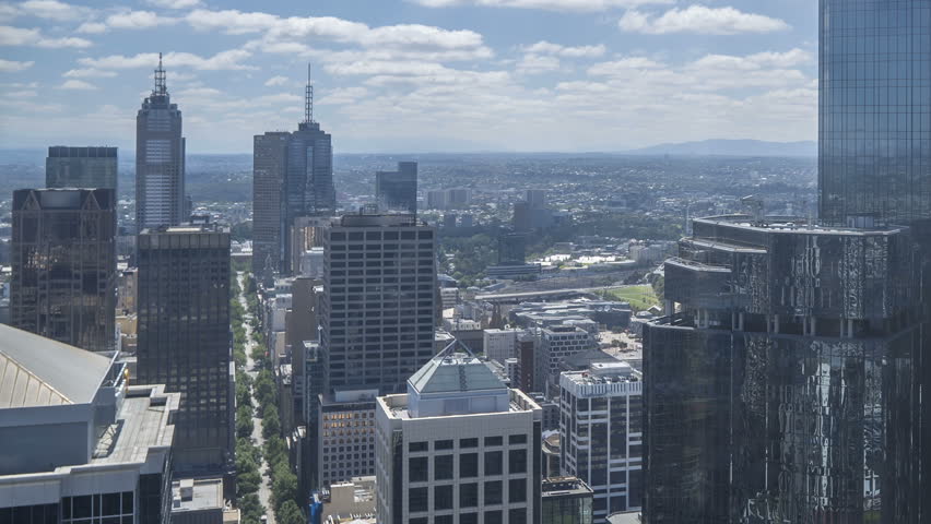 An aerial view of Melbourne cityscape including Yarra River and Victoria Harbour in the distance. Cloudscape time lapse during day light time with moving clouds. Zoom out