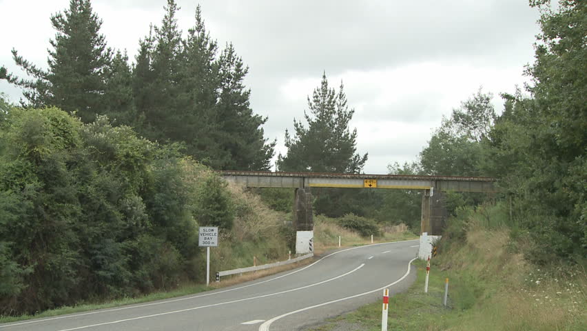 A steam train and carriages pass over a road bridge