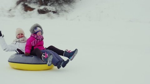 The woman with the child down from a hill on an inflatable circle of Tube. Laughing, waving their hands in the camera. Winter fun