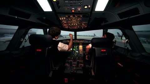 Two caucasian male pilots in the cockpit or flight deck of a passenger airplane switch controls panel of aircraft and prepare for taxiing on the runway before take off on Airbus A319 A320 A321