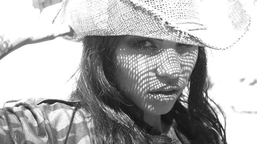 Video of beautiful woman in camouflage jacket and straw hat smiling on a sunny day. Face closeup of pretty girl with straw hat pattern shadow on her face - black and white video in slow motion