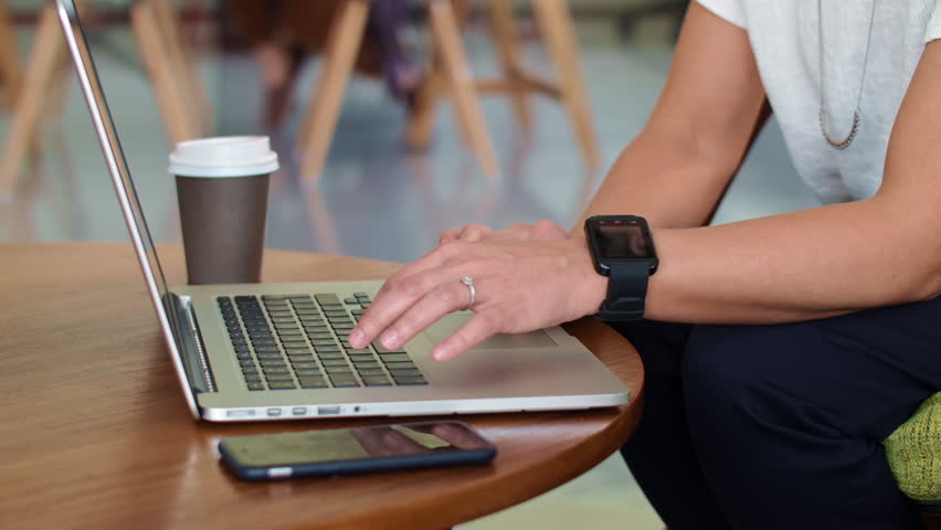 busy business woman typing on laptop stops and scrolls through urgent alerts on smart watch device