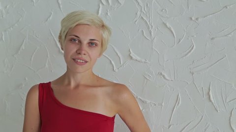 Pretty, young and blonde woman in red dress without make-up looking at camera. White background. Natural beauty concept