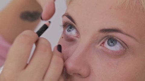 Professional make-up artist applying eyeliner around the entire eye of model in white room. Beauty, makeup and fashion conceptin white room. Beauty, makeup and fashion concept