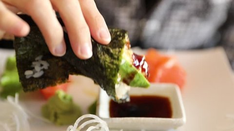 Slow motion focus on hand eating a California Temaki cone with shrimp tempura, rice, avocado and seaweed, in soy sauce bowl. Japanese fusion food, Asian cultures. Healthy food, light diet concept.