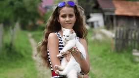 Girl in blue sunglasses holds in hands white cat. Pretty girl holds in hands white cat and looks at the camera. Unique cat has one blue eye and one yellow eye, it is seen in high resolution video
