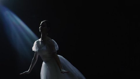 Mid Shot of a Beautiful Young Ballerina Spinning Gracefully in the Spotlight. She Throws Dust Particles in the Air They Shine in the Darkness Around Her. Shot on RED EPIC-W 8K Helium Cinema Camera.