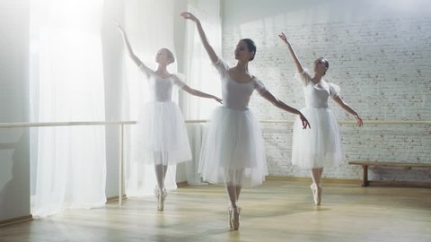 Three Young and Gorgeous Ballerinas Synchronously Dancing. They Wear White Tutu Dresses. Shot on a Sunny Morning in a Bright and Spacious Studio. Shot on RED EPIC-W 8K Helium Cinema Camera.