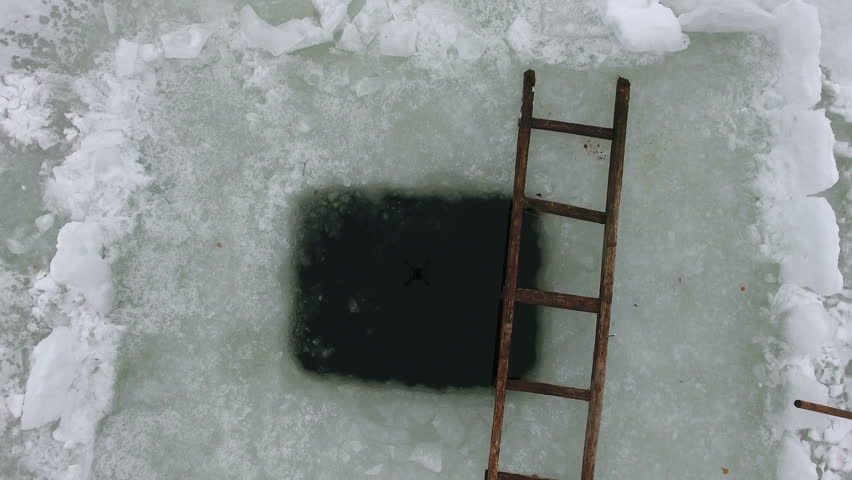Camera flying up over squared ice-hole in ice of winter forest lake, nobody