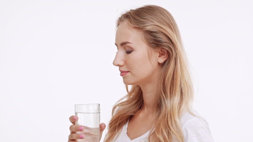 Young beautiful Caucasian blonde girl drinking water from glass and smiling at camera. Profile view on white background in slowmotion | Shutterstock HD Video #23347480