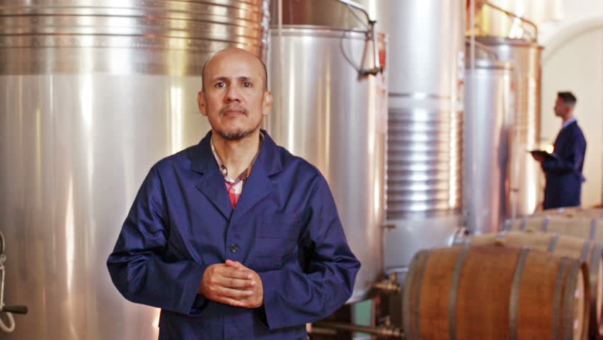 Portrait of mature male cheerful winery worker standing on wine factory in   fermentation section 