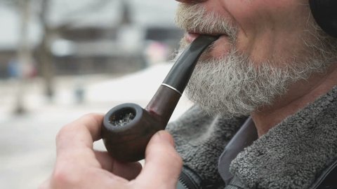 Close-up of smoking man holding a tobacco pipe outdoors