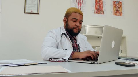 Concentrated Afroamerican young doctor using laptop at his desk