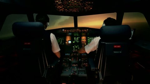 Modern passenger plane change course and start to descent. Sunset view from the cabin of modern plane to the Airport ruway with lighting. Two professional male pilots in the cockpit or flight deck