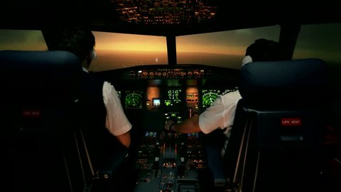 Modern passenger aircraft during descent. Sunset view from the cabin of modern plane to the Airport ruway with lighting. Two professional male pilots in the cockpit or flight deck control airplane