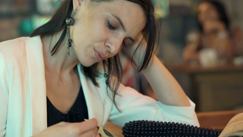 Young, elegant woman reading menu sitting in cafe at night
