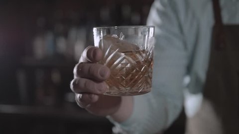 Hand holding a glass of whiskey on the rock in bar. Man shake alcohol in bar.