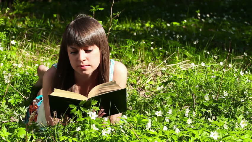 beautiful girl reading a book in forest on flowers field
