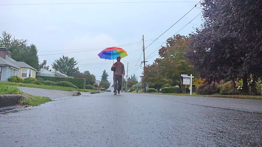 Young man in rain with multi colored umbrella, walking towards and away from