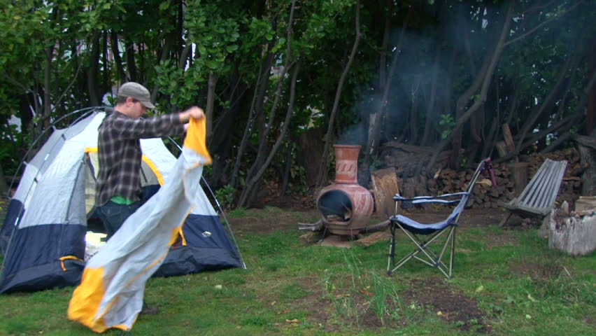 Man sets up campsite with tent and makes fire in backyard with his pet cats