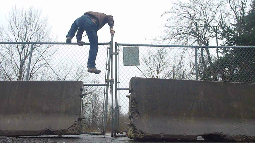 Man with skateboard jumps over cyclone fence and enters private property.