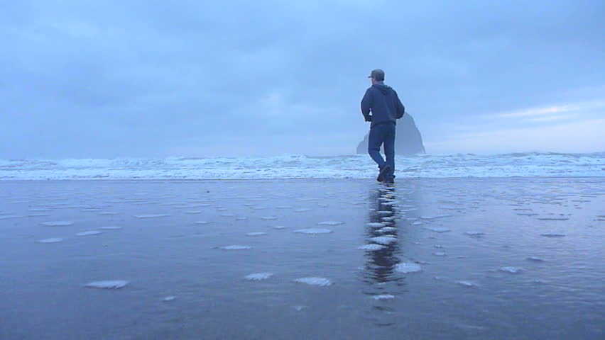 Man walking on sandy beach to the Pacific Ocean in Oregon's coastline during