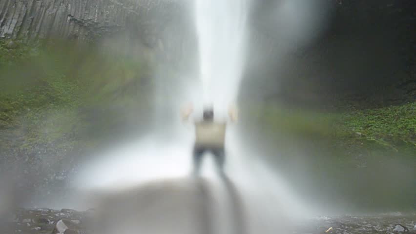 Man walking near large waterfall in Oregon on rainy day reaches falls and lifts
