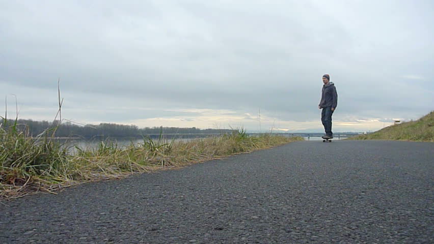 Man skateboards towards camera on path along river in Portland, Oregon.