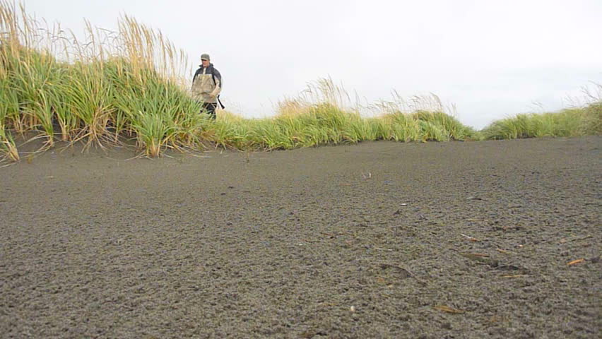 Man walking toward camera on stormy day near Pacific Ocean.