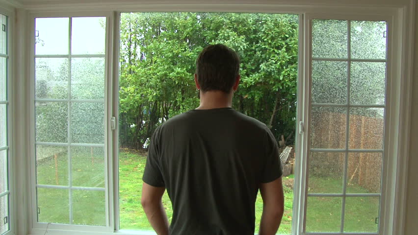 Man looking out window watching heavy wind and rain during storm.