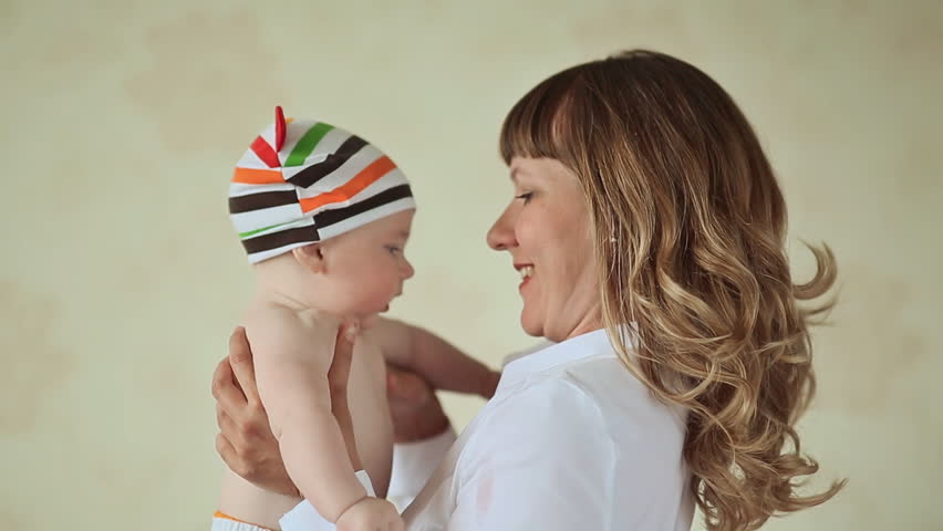 Loving mother playing with her baby. Dressed baby in striped shorts and cap.