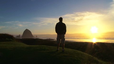 Man at Pacific Ocean near Cannon Beach looks out to sea as sun sets on beautiful day.