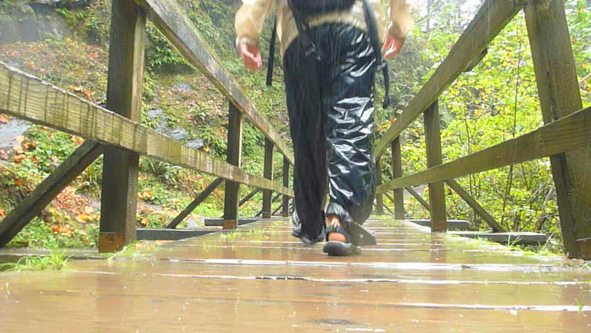 Man in Oregon forest hikes down wooden bridge during rain storm with raincoat