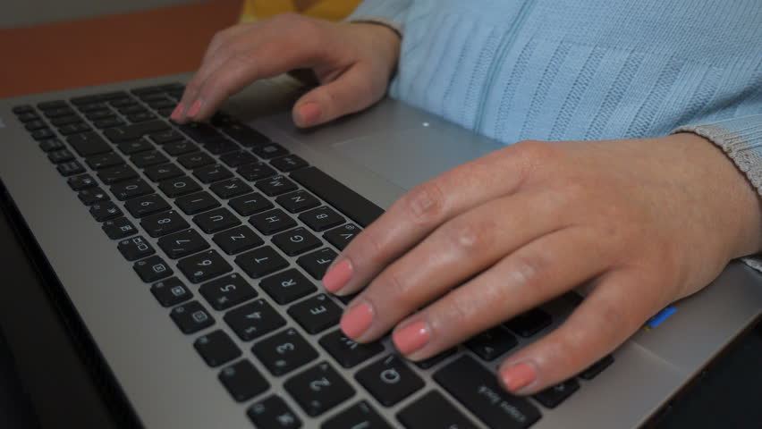 Young woman sitting on the couch and using notebook. Camera moves from the keyboard up to her face. Crane shot.