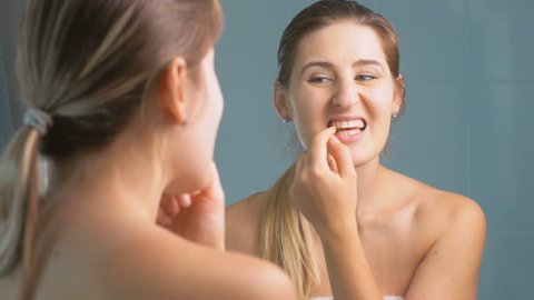 4K footage of young woman checking her teeth at mirror in bathroom